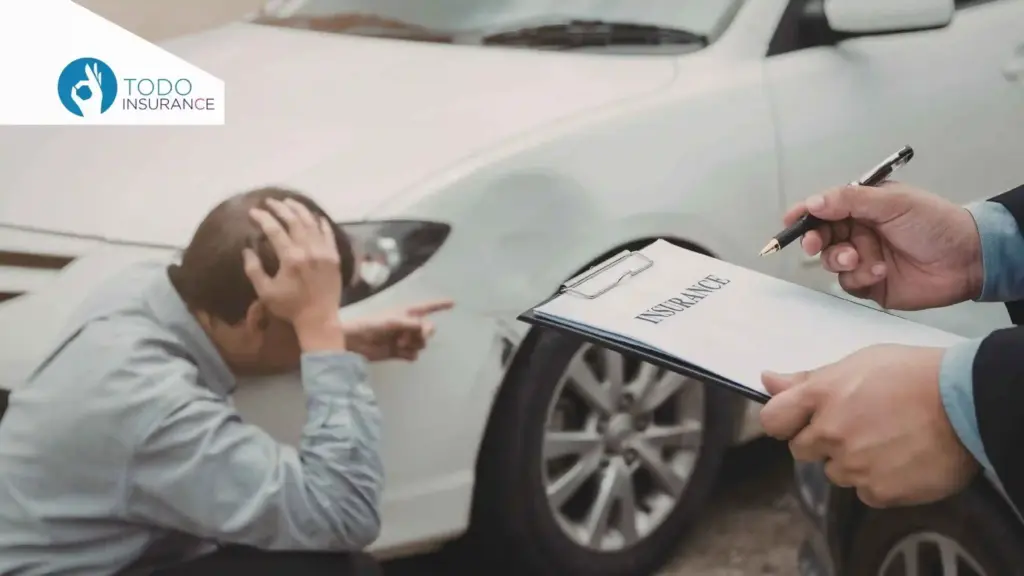 unas manos sostienen una tabla con un documento que dice insurance y un esfero un hombre està agachado con una mano en la cabeza y otra señalando un golpe sufrido por un carro blanco Qué Factores Afectan el Precio del Seguro de Auto todo insurance