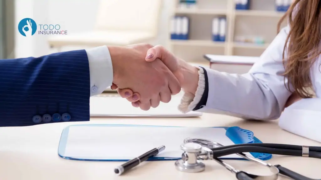 Persona da la mano a una profesional medicó sobre la mesa hay documentos un esfero y un estetoscopio qué es obama care todo insurance