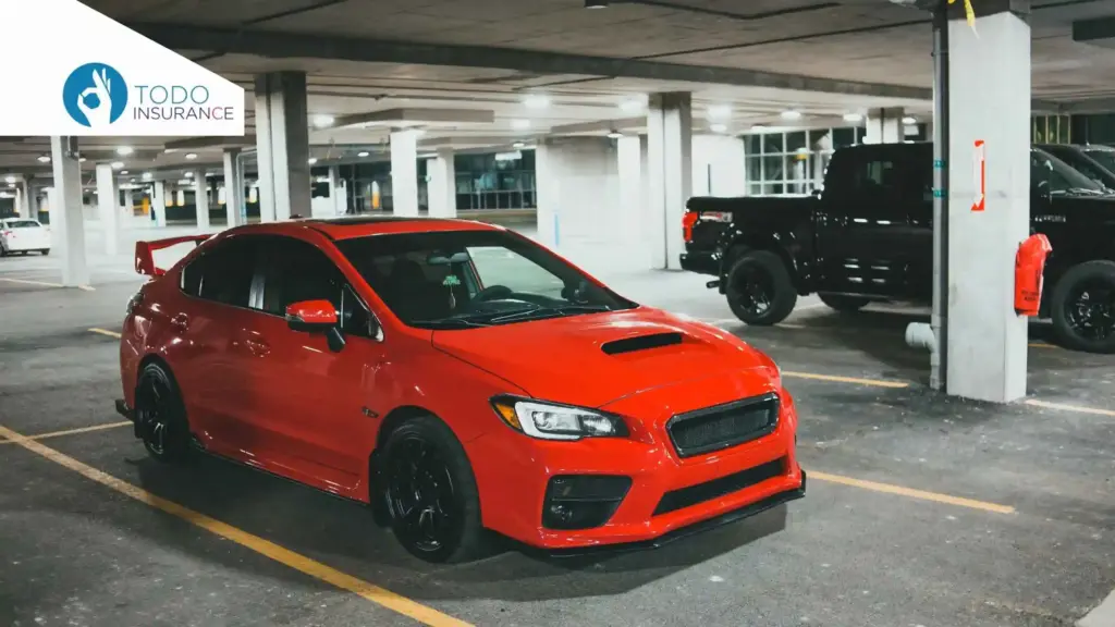 auto rojo en un un parqueadero de columnas blancas al fondo una camioneta oscura de planton Qué Factores Afectan el Precio del Seguro de Auto todo insurance